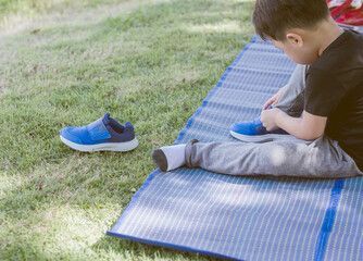 Little asian boy wearing shoes by himself in park. Life skills, Sport day concept. Copy Space.