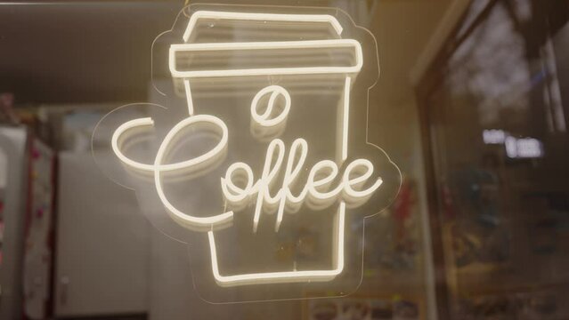 A handwritten coffee logo on a wooden facade in the darkness, with a neon sign illuminating the grass. The art deco font stands out on the metal rectangle