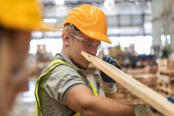 Man wearing safety uniform and yellow hard hat working checking quality wooden products at workshop...