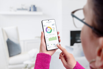 Woman uses electricity usage app for consumption monitoring and analysis in living room. Concept of...