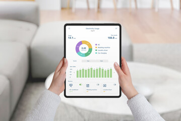 Hands holding tablet with home electricity monitoring app, analyzing consumption by device and month. Concept of energy efficiency and data tracking