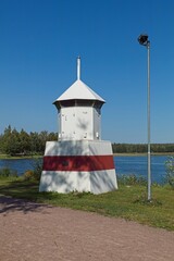 A red and white beacon standing on lake shore in summer.