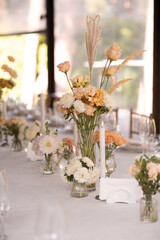 A large, long, decorated, wooden table and chairs, covered with a white tablecloth with dishes, flowers, candles.