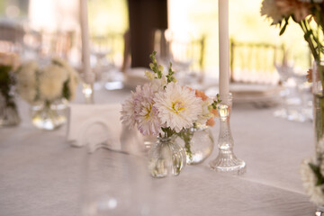 A large, long, decorated, wooden table and chairs, covered with a white tablecloth with dishes, flowers, candles.
