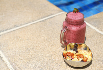 Berry Smoothie and Mixed Nuts by the Poolside. A jar of berry smoothie and a dish with mixed nuts rest on a poolside. Horizontal photo