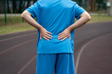 Back pain, kidney inflammation, man suffering from backache on a sports ground after workout - 754200376