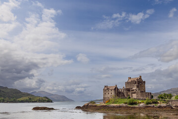 The storied Eilean Donan Castle presides over a peaceful loch, its image set against the lush greenery of the Highlands under a vast, expressive sky