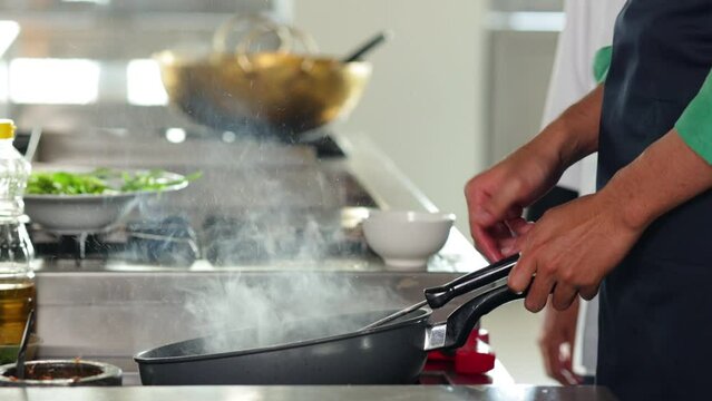 Thai Asian man professional chef cooking meal with fire at kitchen restaurant. culinary classroom. cooking school. cooking lessons in a cooking school.