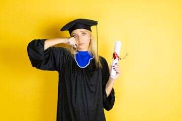 Beautiful blonde young woman wearing graduation cap and ceremony robe depressed and worry for...