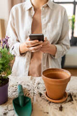 people, gardening and planting concept - close up of woman with smartphone and pot flower at home - 754222934