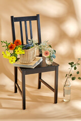 home decor and design concept - close up of flowers in basket, vases and glass bottle and magazines on vintage chair over beige background - 754224385