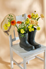 gardening, international women's day and floral design concept - flowers in rubber boots and straw hat on vintage chair over beige background - 754224567