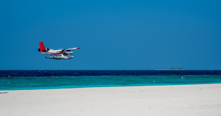 Seaplane fly low above sea level by the sandy beach.