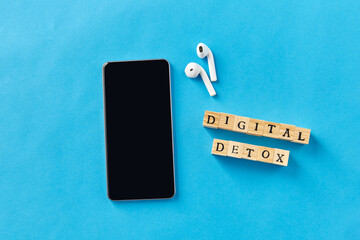 digital detox and technology concept - smartphone, wireless earphones and wooden toy block or stamps on blue background - 754225571