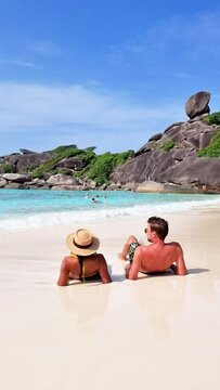 A couple is relaxing on a beach, gazing at the beautiful ocean under the clear sky. The tranquil natural landscape brings peace and leisure to their travel experience Similan Islands, Thailand