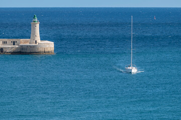 A boat enters the Grand Harbour of Valletta with the St. Elmo breakwater lighthouse in the...