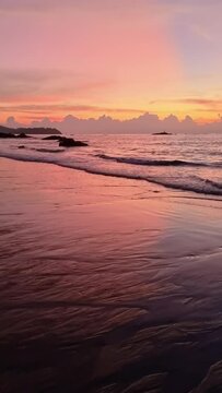 The sky painted in hues of red and orange as the sun sets over the beach, casting a tranquil afterglow on the fluid water and crashing waves at dusk Khao Lak Thailand