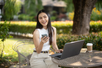 Young woman uses smartphone while working with laptop at outdoor cafe and coffee.