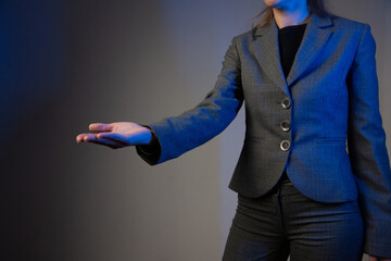 Part of a business woman with her arm extended forward and palm up. Gray background. Blue color correction. Side view