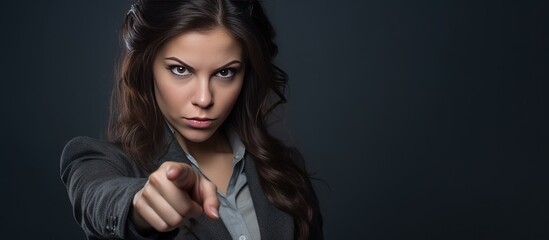 A woman with a serious expression pointing a gun directly at the camera on a grey background.