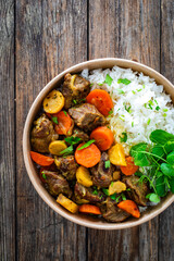 Takeaway food - roast pork with carrots and celeriac in sauce with white rice in lunch box on wooden table
