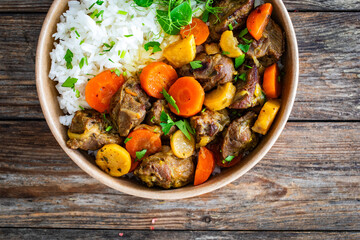 Takeaway food - roast pork with carrots and celeriac in sauce with white rice in lunch box on wooden table
