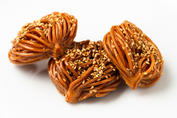 Three pieces of traditional Moroccan pastry, chebakia or bouchnikha, coated in syrup and adorned with sesame seeds, presented on a pure white background