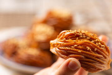 A hand delicately holds a Bouchnikha, a traditional Moroccan sweet made of fried dough shaped like...
