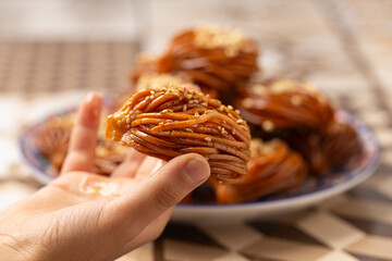 Close-up of a hand presenting a Chebakia, a beloved Moroccan pastry symbolizing festivity. Its intricate flower-like design, honey glaze, and sesame seeds make it a cherished delight during Ramadan an