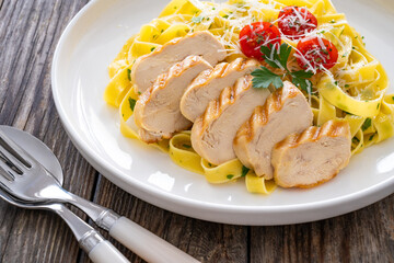 Grilled sliced chicken breast and pappardelle noodles on wooden background
 - obrazy, fototapety, plakaty