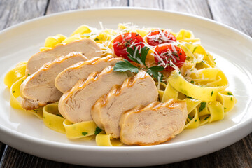 Grilled sliced chicken breast and pappardelle noodles on wooden background
