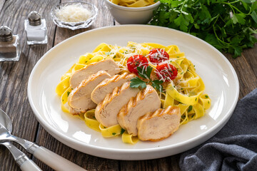 Grilled sliced chicken breast and pappardelle noodles on wooden background
