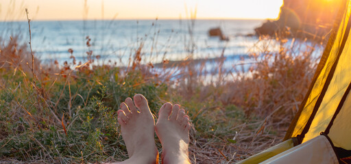 woman legs stick out from a tent at dawn on the sea coast. Outdoor recreation, Travel and tourism....