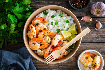 Fried shrimps with boiled white rice and lime in lunch box to go on wooden table
