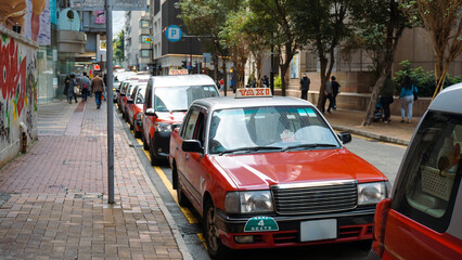 A fleet of Hong Kong taxis waiting at a taxi stand. Hong Kong taxis are easily recognizable by their red and white colors. - obrazy, fototapety, plakaty