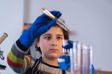 A cool teenager in a home research laboratory wearing safety glasses and rubber gloves is concentrating on an experiment on mixing liquids. Advanced school science project - obrazy, fototapety, plakaty