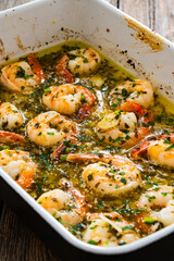 Fried shrimps with parsley and garlic in olive oil in cooking pan on wooden table
