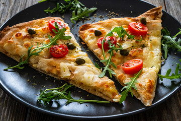 Roman pinsa slices with mozzarella cheese, capers, arugula and garlic on wooden table

