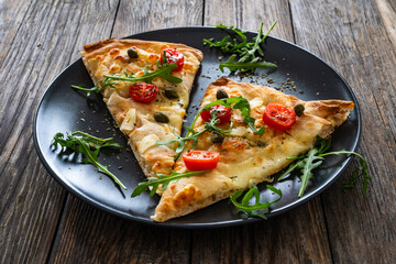 Roman pinsa slices with mozzarella cheese, capers, arugula and garlic on wooden table
