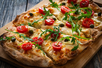 Roman pinsa with mozzarella cheese, capers, arugula and garlic on wooden table
