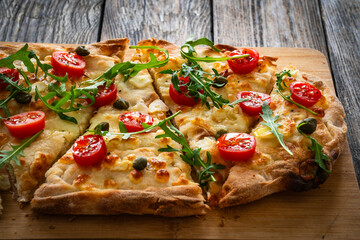Roman pinsa with mozzarella cheese, capers, arugula and garlic on wooden table
