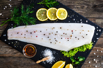 Fresh raw halibut fillet with lemon and dill on black stony  cutting board on wooden table
