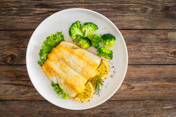 Seared halibut fillet, sliced lemon and boiled broccoli on wooden table
