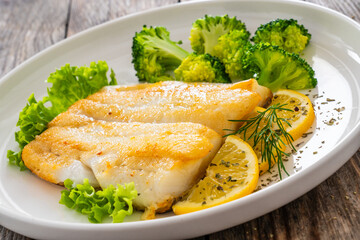 Seared halibut fillet, sliced lemon and boiled broccoli on wooden table
