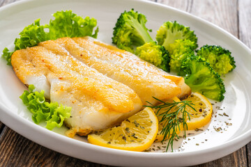 Seared halibut fillet, sliced lemon and boiled broccoli on wooden table
