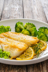 Seared halibut fillet, sliced lemon and boiled broccoli on wooden table
