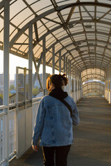 A photo of a girl from behind walking across a pedestrian bridge at sunset and looking to the left