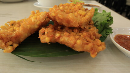 Crispy fried corn balls in white plate on wooden table, vegetarian food.