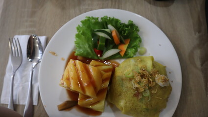 A plate of pattaya fried rice with fried chicken pieces of fruit and vegetables served on a white plate