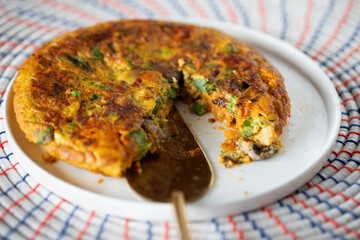 VEGETABLE FRITTATA CLOSE UP ON WHITE PLATE ON WOVEN AFRICAN MATT GOLD SERVING SLICE 